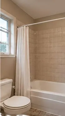 Guest bathroom before: tub with a shower curtain and beige tile